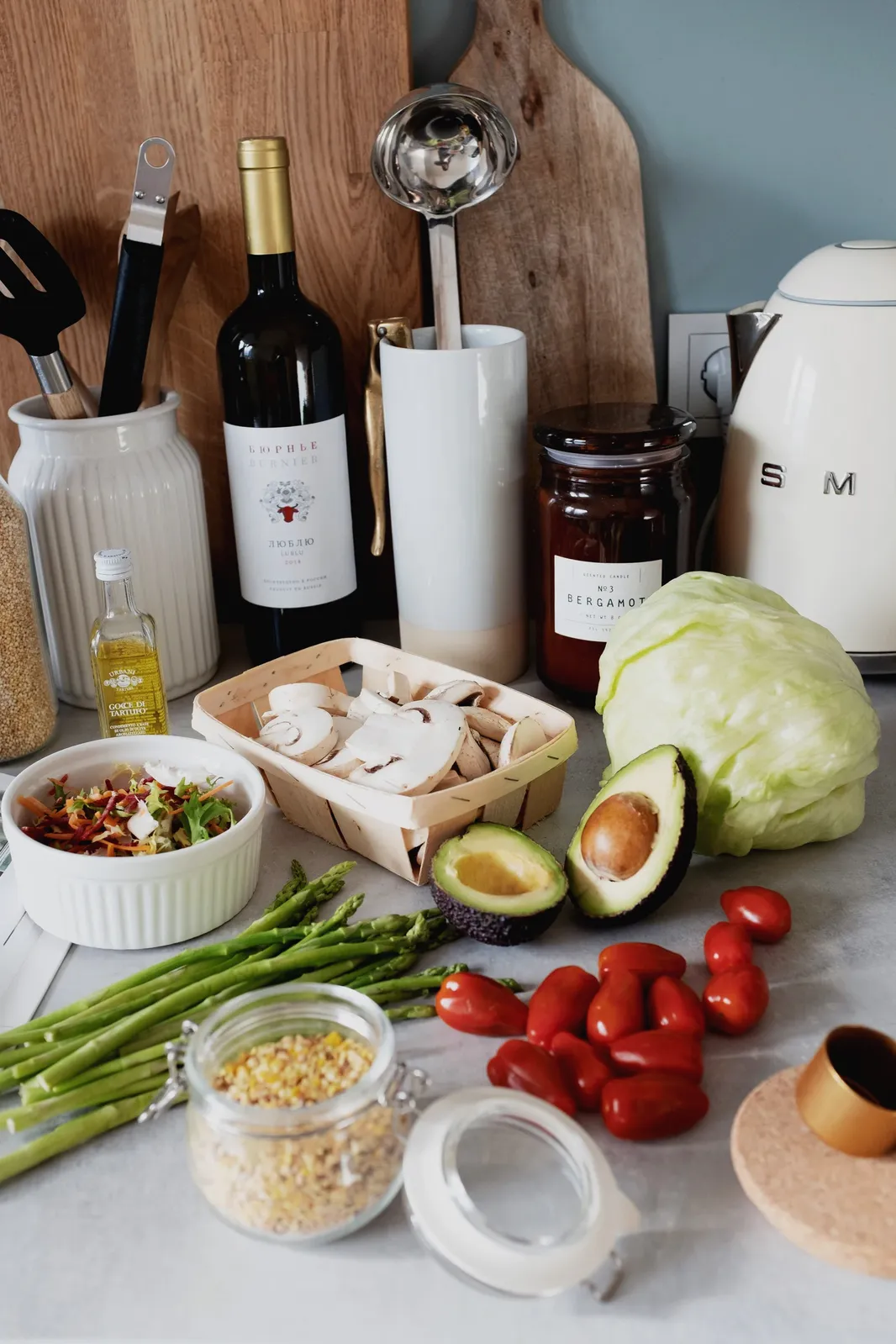A kitchen counter with sliced mushrooms, avocado, cabbage, asparagus, and jars and bottles of pantry staples